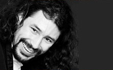A black-and-white face portrait of a smiling Mitch with his long, black curly hair.